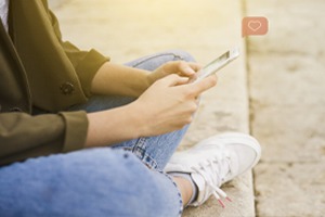 woman sitting on the side walk crossed legged looking at her phone.